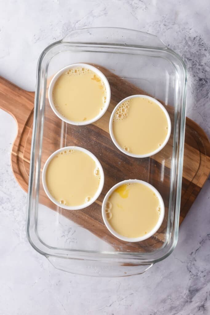Mixture of jericallas served in small white containers placed inside a large glass baking dish and in bain marie.