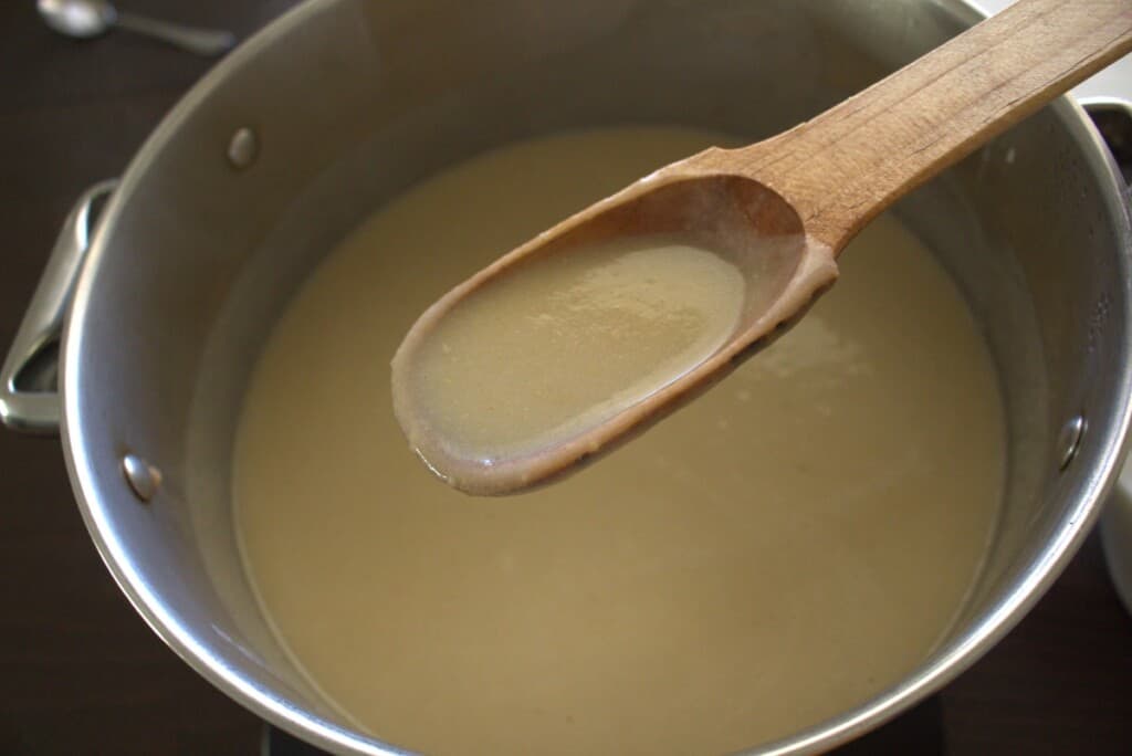 A wooden spoon with the atole mixture over the pot.