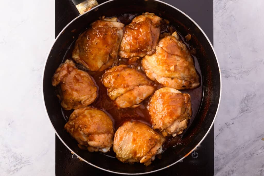 Adding chicken thighs to a large skillet with sauce.