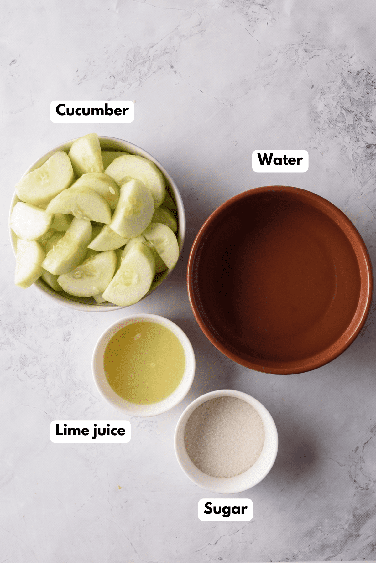 The ingredients needed to make Agua de Pepino labeled and sitting on a white marble surface.