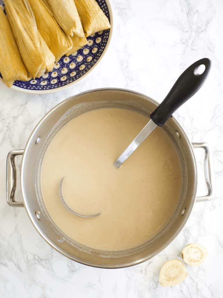 Freshly made Mexican guava atole in a pot with tamales on a blue plate next to the pot.