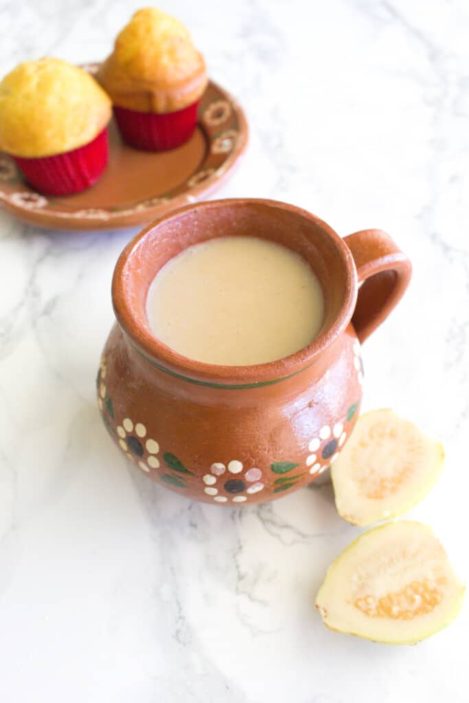 Atole de guayaba (or Guava Atole) served in a mug next to Mexican sweet breads.