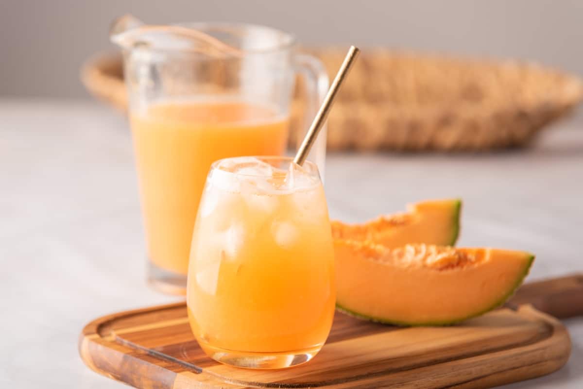 Cantaloupe Agua Fresca served in a glass with a straw next to fresh fruit.