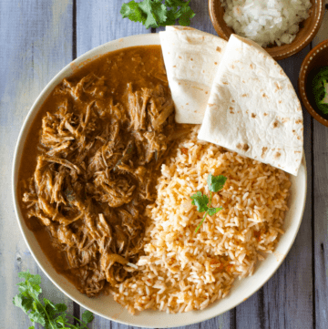Carne deshebrada served on a plate next to Mexican rice and two flour tortillas.