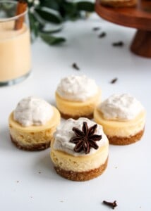 Rompope Cheesecake Bites topped with star anise with a glass of eggnog in the background.