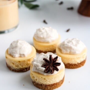 Rompope Cheesecake Bites topped with star anise with a glass of eggnog in the background.