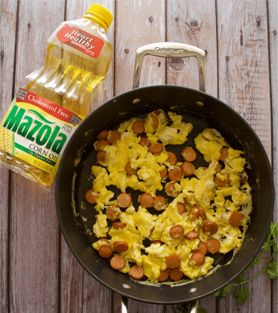 A large skillet with huevos con salchicha next to a bottle of oil.