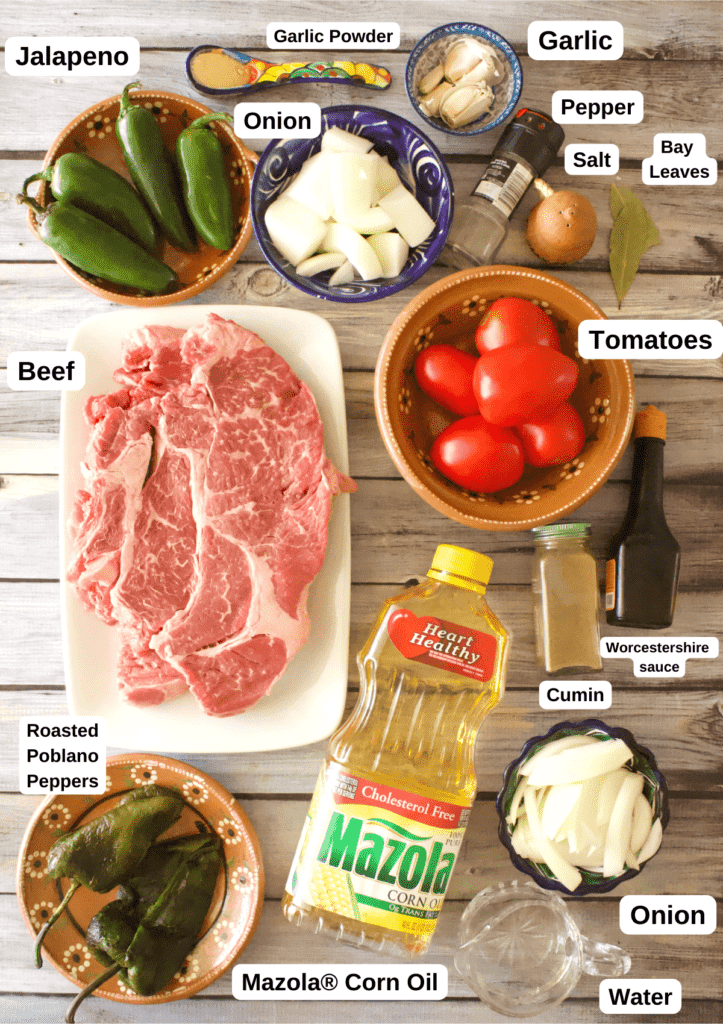 The ingredients needed to make Carne Deshebrada, or Mexican Shredded Beef, labeled and sitting on a wooden surface.