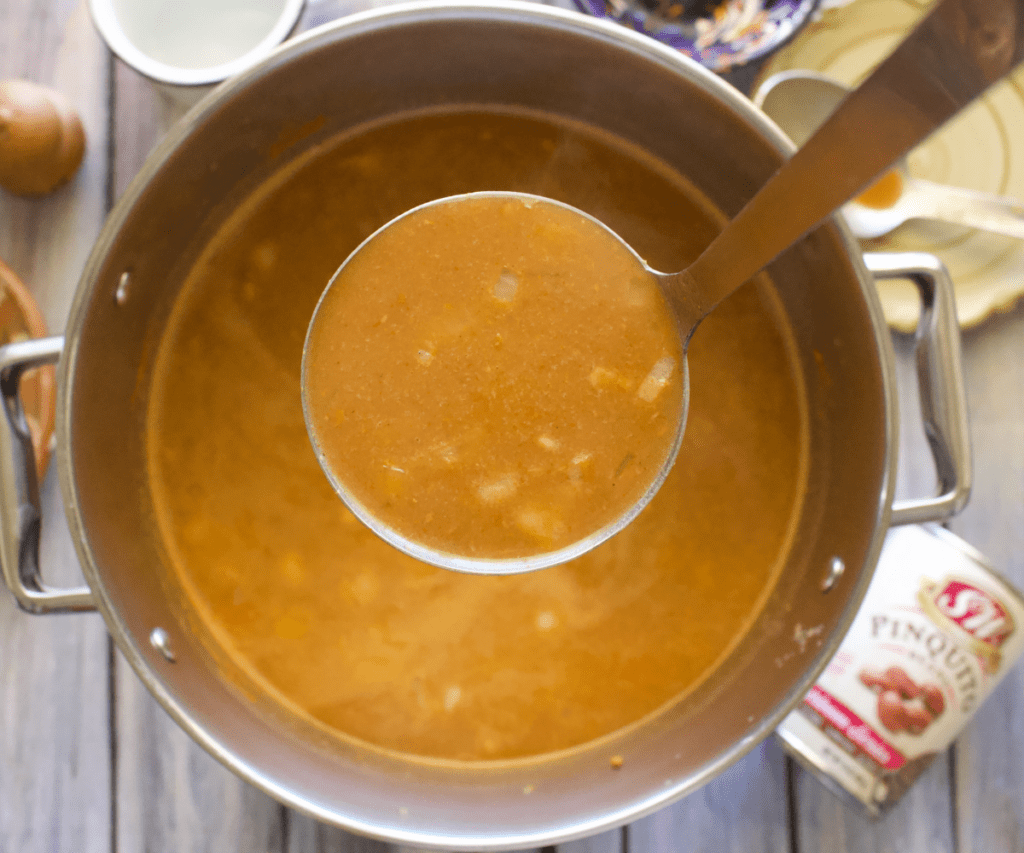 A ladle of the bean soup over a pot of soup.