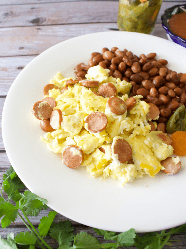 Huevos con Salchicha served on a white plate next to refried beans and pickled jalapenos.