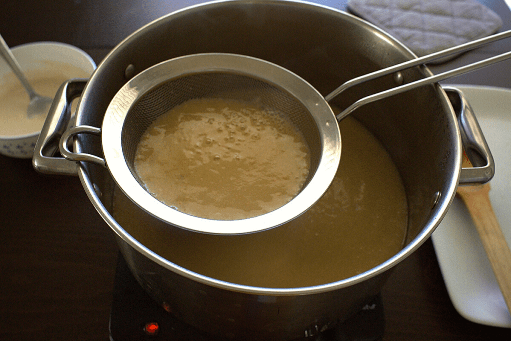 Straining the guava puree mixture into the pot.