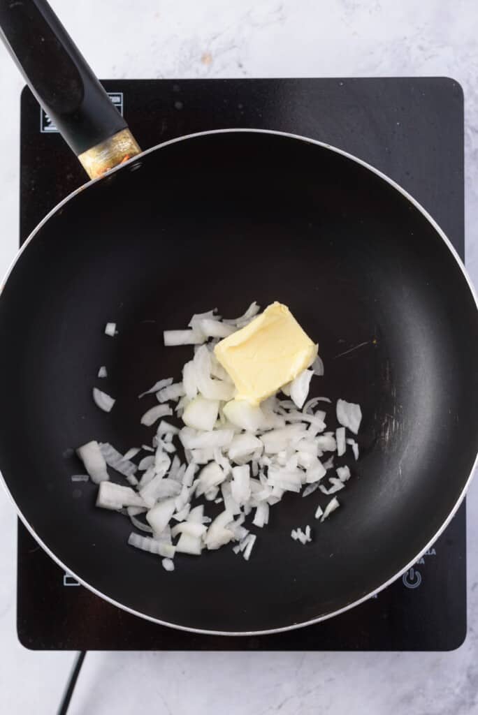 A large nonstick skillet with butter and diced onion.