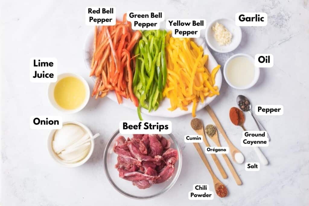 The ingredients needed to make Beef Fajitas labeled and sitting on a marble surface.