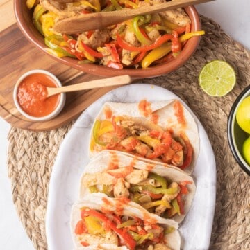 Fajitas de Pollo Tacos served on a white plate next to lime and tomato salsa.