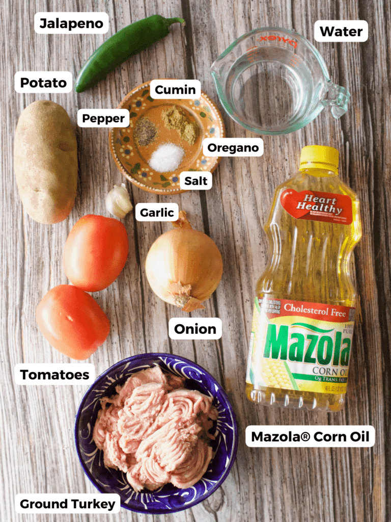 The ingredients needed to make turkey picadillo labeled and sitting on a wooden surface.