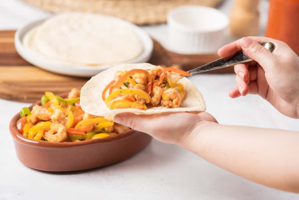 A hand holding a flour tortilla and assembling fajitas de camaron.