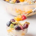 A spoonful of the creamy Mexican fruit salad over a small bowl.