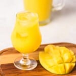 Agua de Mango served with ice next to a fresh mango on a wooden cutting board.