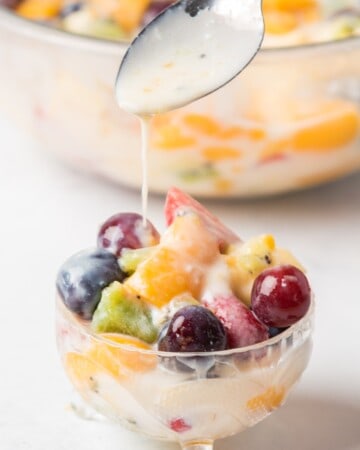 A spoon drizzling the creamy sauce over the fruit salad.