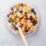 Creamy Mexican Fruit Salad in a large mixing bowl with a wooden spatula.