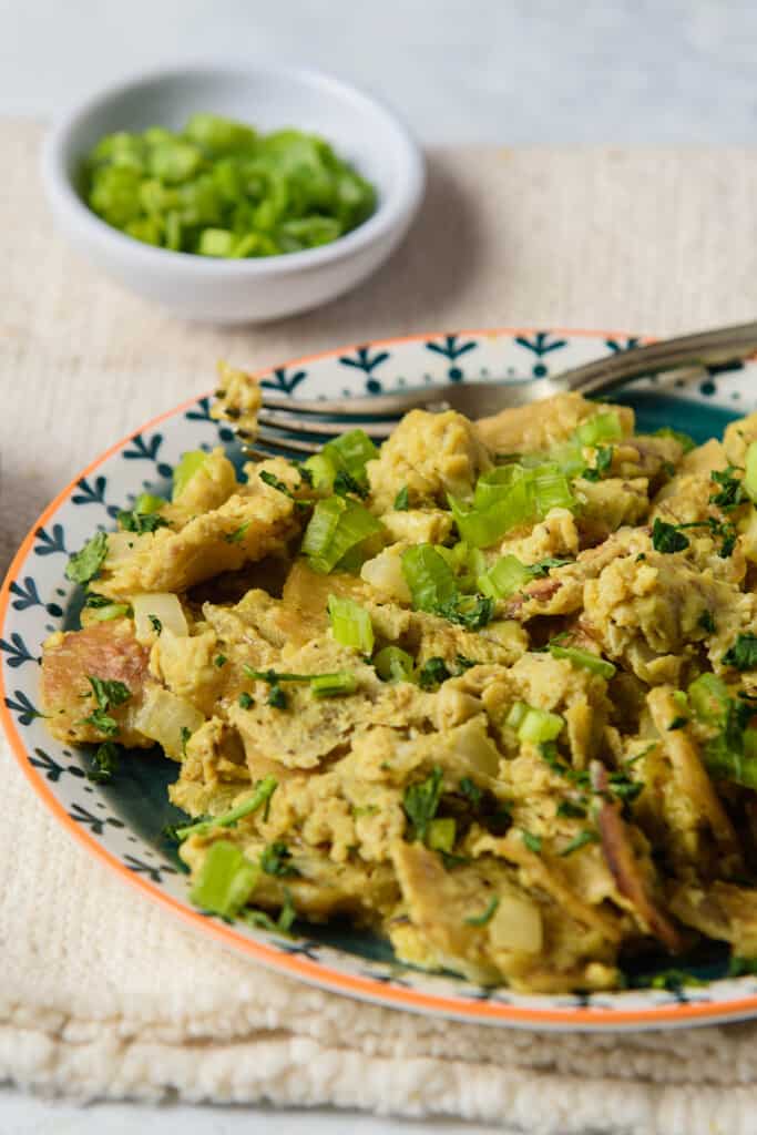 A decorative plate of migas con huevo with a fork next to a small bowl of green onions.