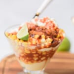 Elote en vaso served in a glass cup with a lime wedge.
