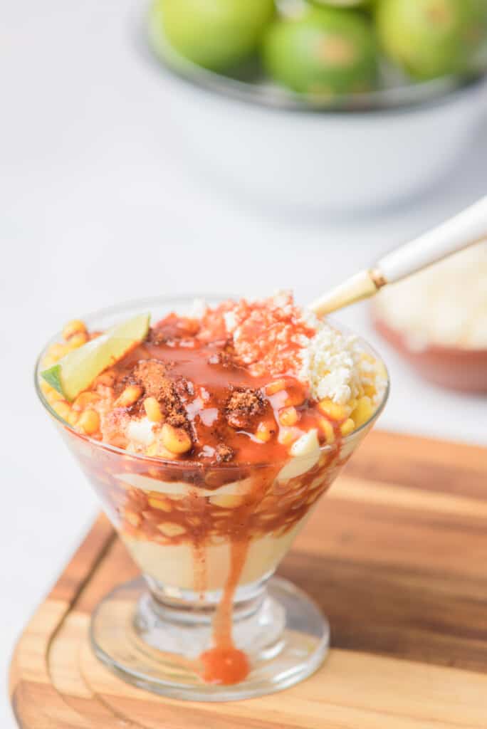 Elote en vaso (or esquites) topped with cheese, chile powder and hot sauce