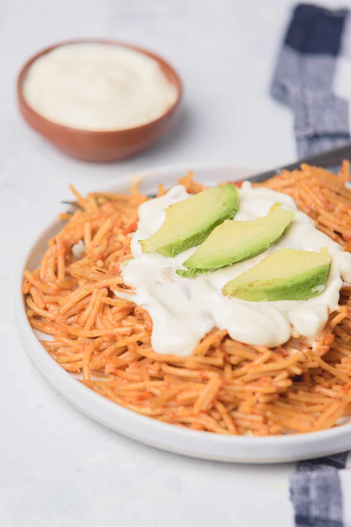 Fideo seco served on a large white plate and topped with avocado slices and sour cream.