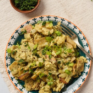 A plate of migas con huevo with a fork next to a small bowl of chopped cilantro.