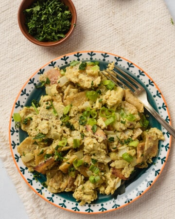 A plate of migas con huevo with a fork next to a small bowl of chopped cilantro.