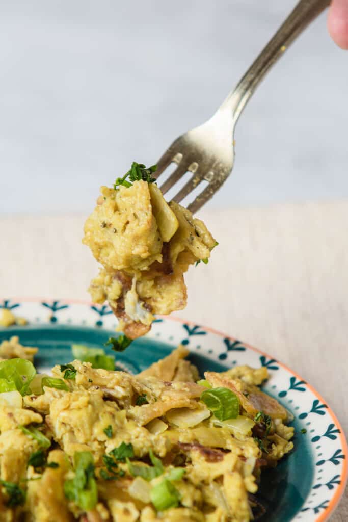 A fork holding migas over a plate.