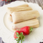 A stack of strawberry tamales (tamales de fresa) sitting on a white plate next to fresh strawberries.