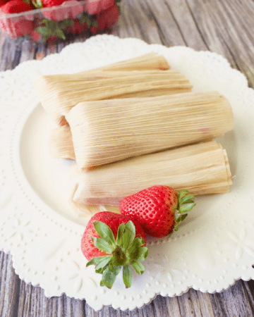 A stack of strawberry tamales (tamales de fresa) sitting on a white plate next to fresh strawberries.