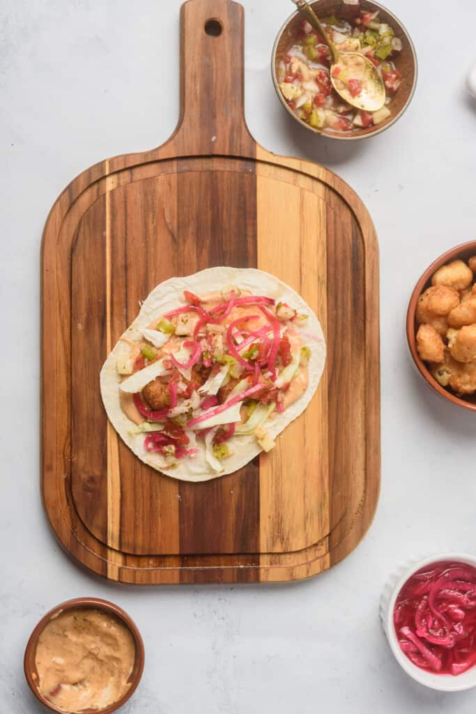 A taco being assembled on a wooden cutting board.