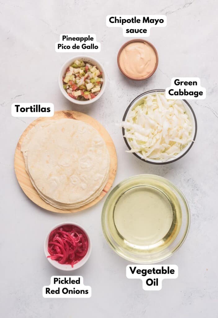 The ingredients needed to assemble Baja Fish Tacos labeled and sitting on a marble surface.