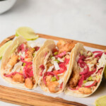 Ensenada-style fish tacos served on a wooden cutting board next to salsa and fried fish.