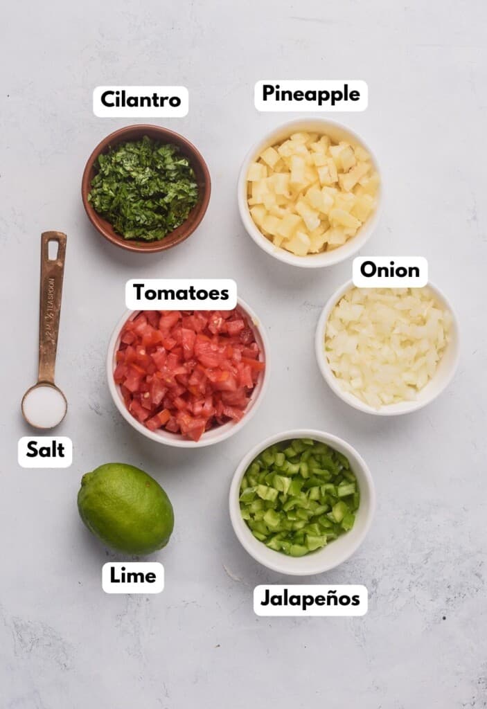 The ingredients needed to make Pineapple Pico de Gallo labeled and sitting on a marble surface.