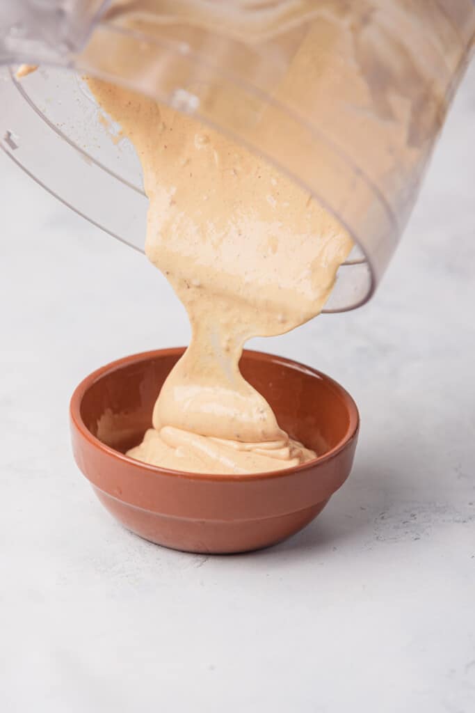Pouring the chipotle mayo sauce into a small clay bowl.