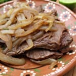 Bistec Encebollado served on a decorative clay plate next to lime wedges.