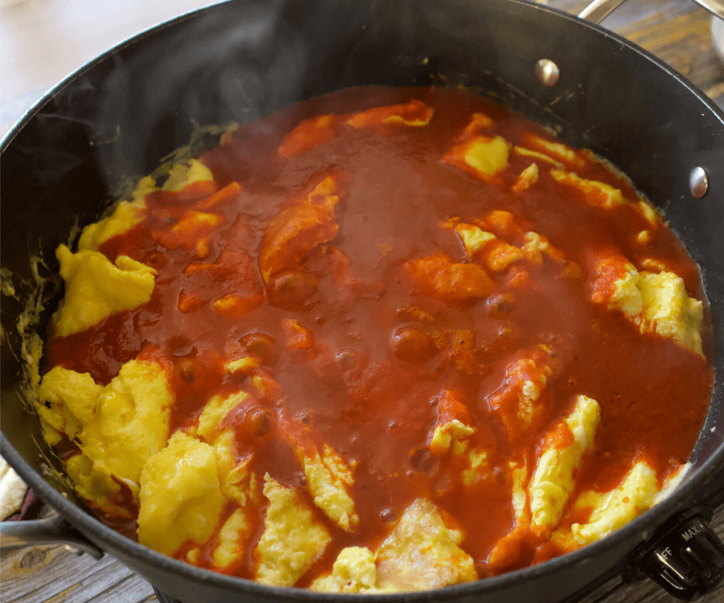 Eggs cooking with the guajillo sauce in a large skillet.