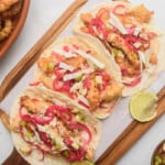 Tacos de Pescado served on a wooden cutting board next to salsa and fried fish.