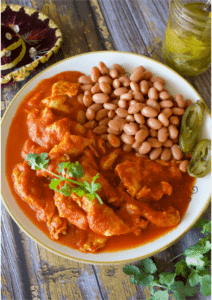 Huevo en Salsa served on a plate next to pinto beans and pickled jalapenos.