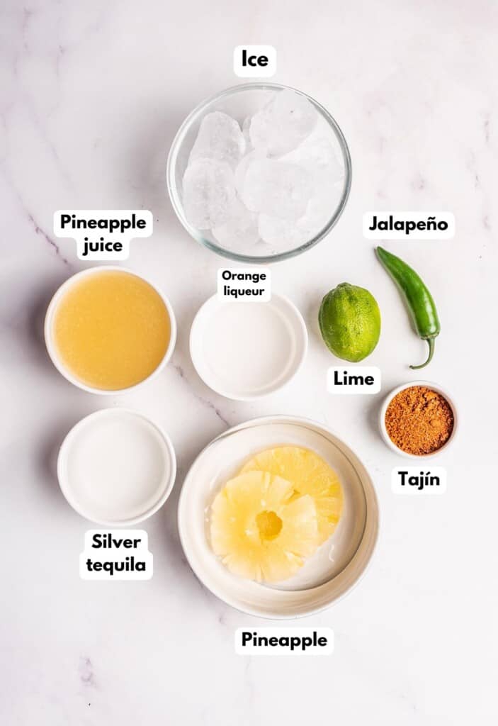 The ingredients needed to make Spicy Pineapple Margarita labeled and sitting on a marble surface.