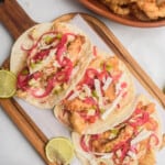 Tacos de Pescado served on a wooden cutting board next to salsa and fried fish.