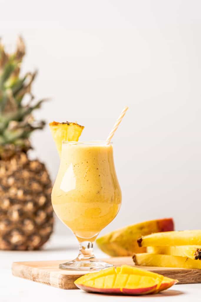 Tropical Mango Pineapple smoothie served in a glass next to mango and pineapple.