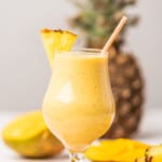 Tropical Mango Pineapple smoothie served in a glass with a straw.