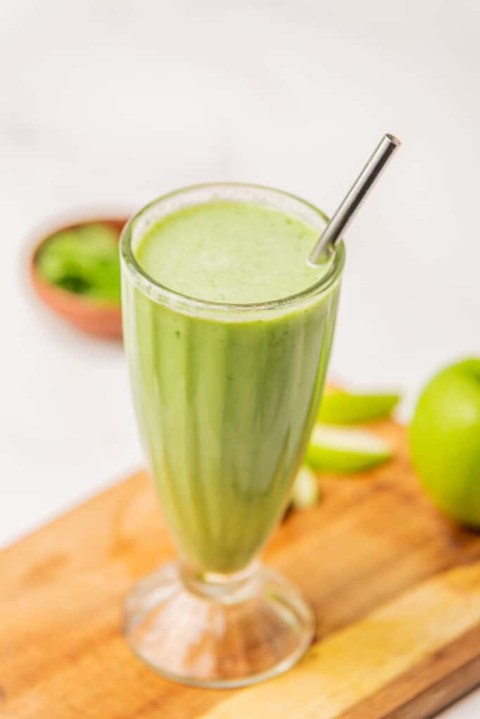 Green Ginger Smoothie served with a metal straw and sitting on a wooden cutting board.