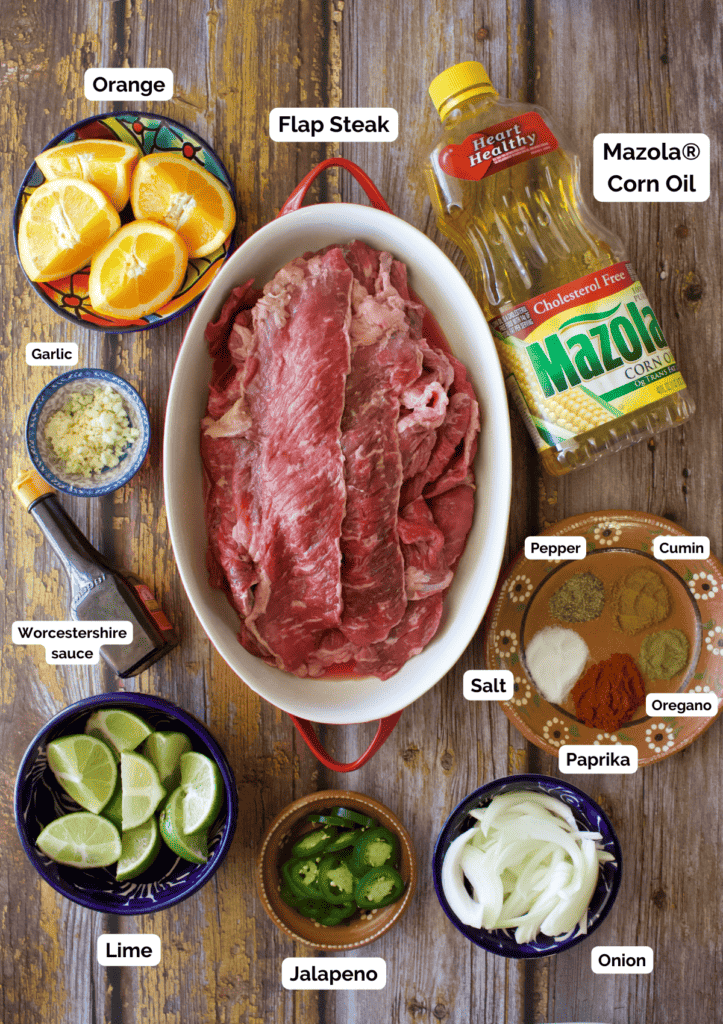 The ingredients needed to make carne asada labeled and sitting on a wooden surface.