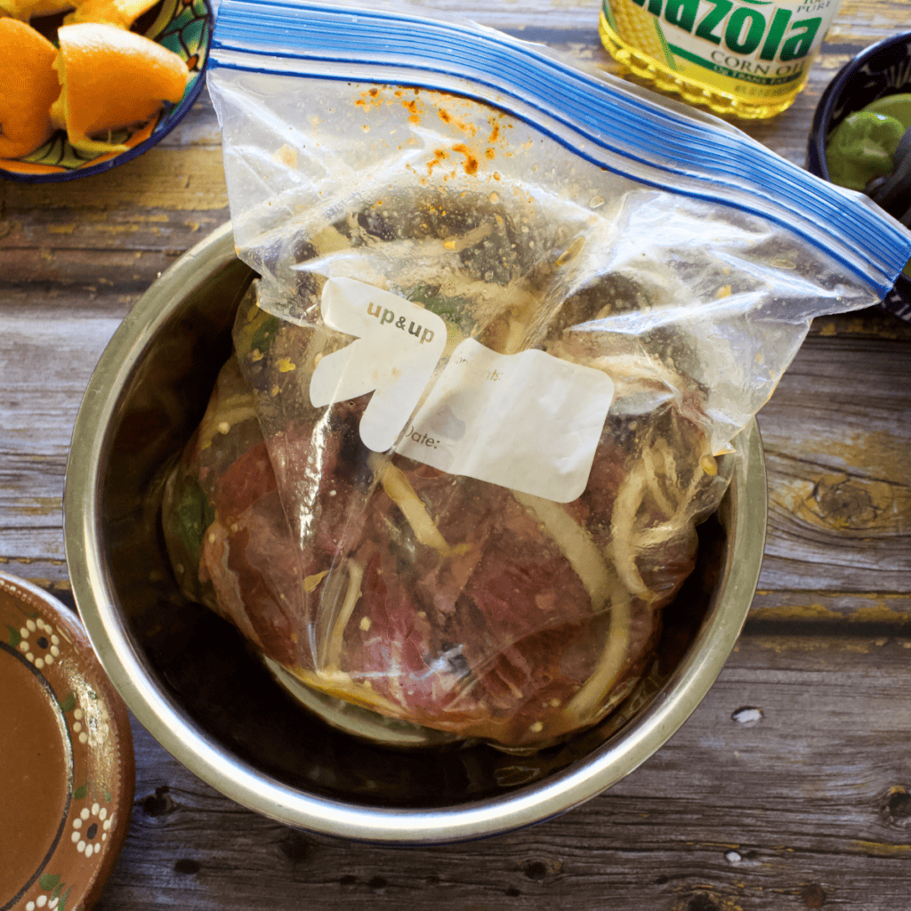Meat marinating in a plastic bag in a metal bowl. 