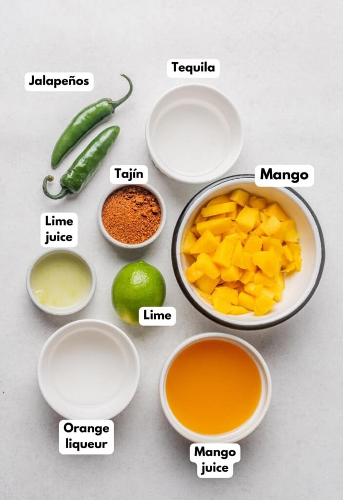 The ingredients needed to make Spicy Mango Margarita labeled and sitting on a marble surface.